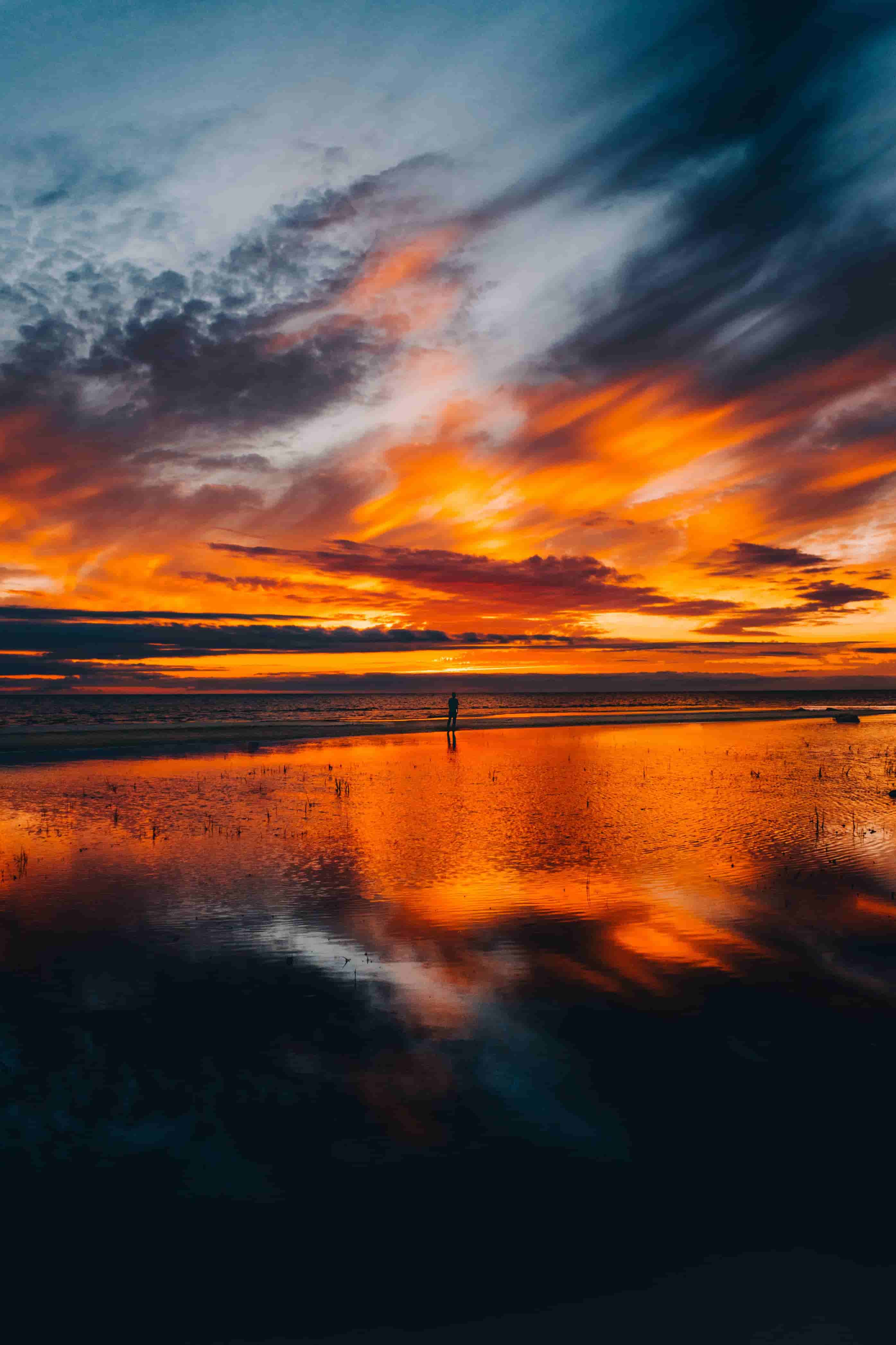 A person is standing on a beach at sunset.